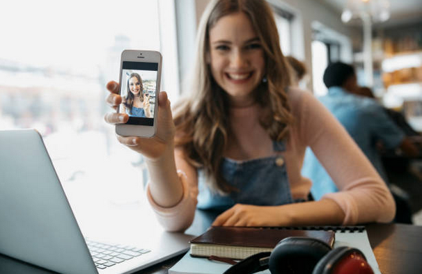 Jeune femme qui sourie en montrant à la caméra un selfie d'elle-même