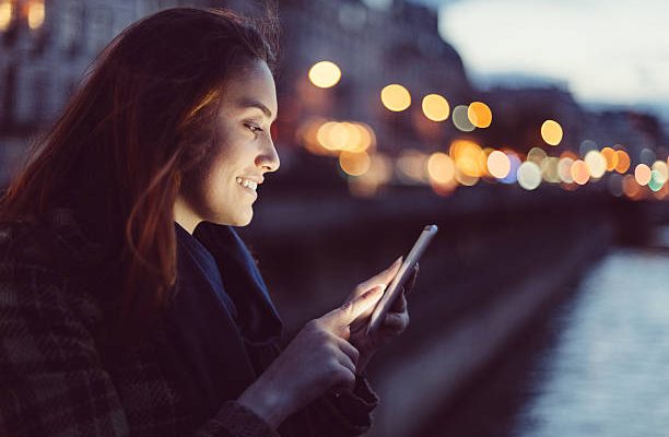 Femme qui envoie un message sur son smartphone à la tombée de la nuit